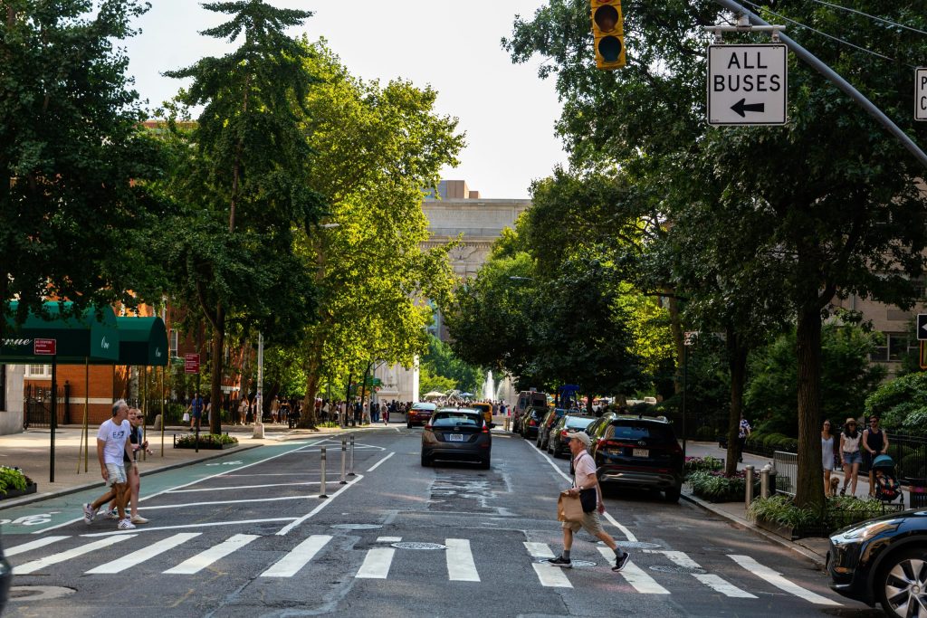 Tree-lined city street with pedestrians and traffic, representing safer roads and walkable communities